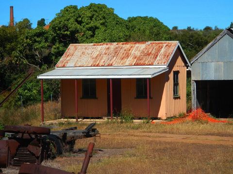 A small corrugated-iron cottage standing among dry grass and trees