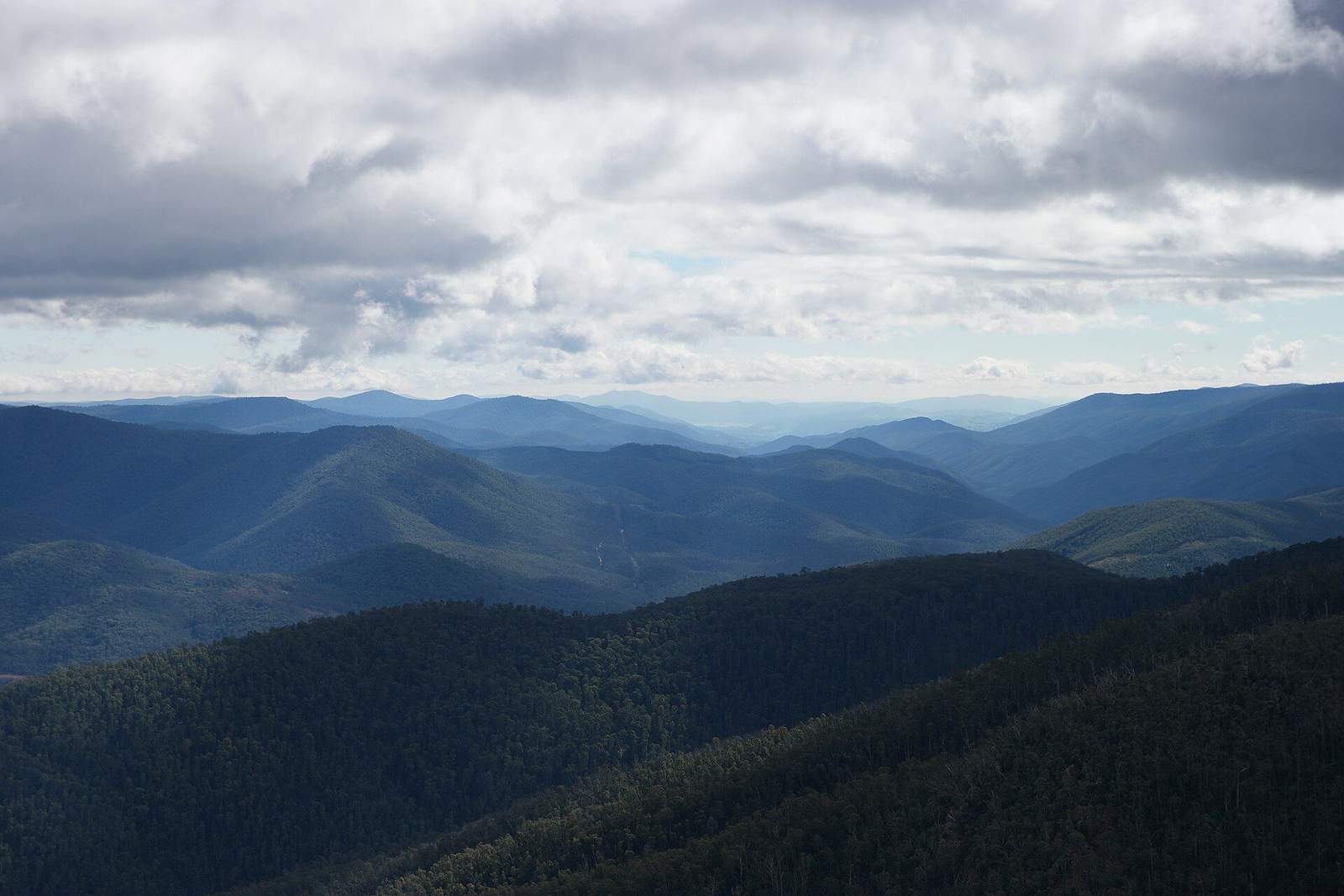 Forested ranges folding away in layers under a wide, cloud-scattered sky