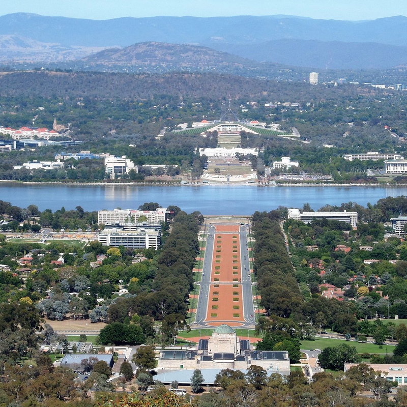 A ceremonial boulevard leading from a domed memorial across a lake toward parliament buildings