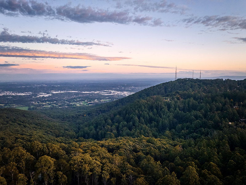 Forested hills falling away toward a distant city under a dusk sky
